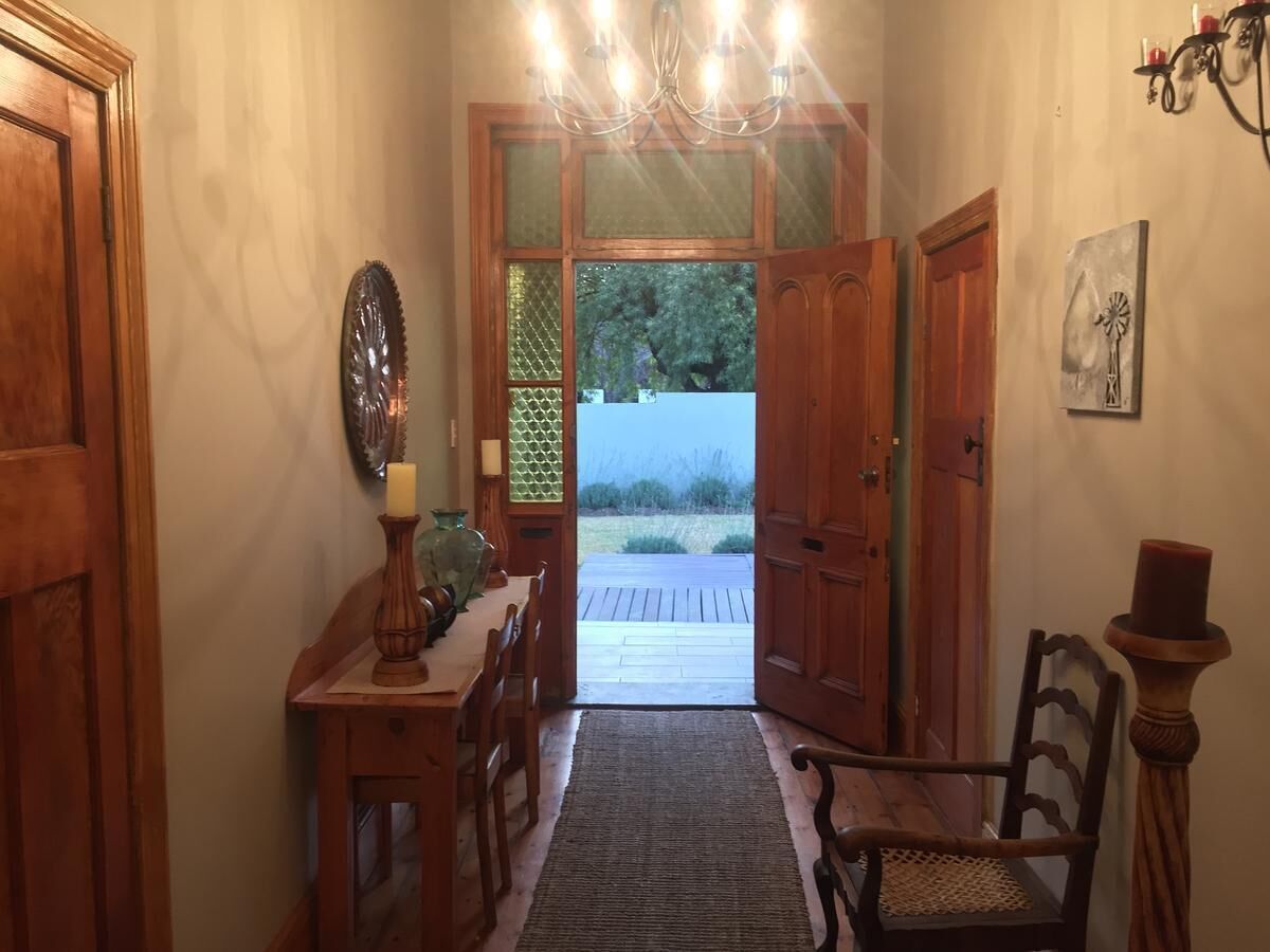 Un pasillo de madera con una araña, una mesa de comedor con sillas y un tapete que lleva a una puerta.