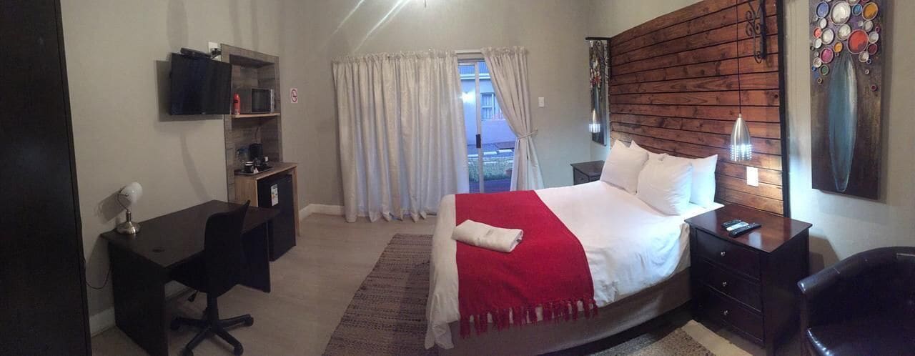Une chambre à coucher comprenant un lit, des tables de chevet, un bureau, une chaise, un téléviseur et une fenêtre avec des rideaux.