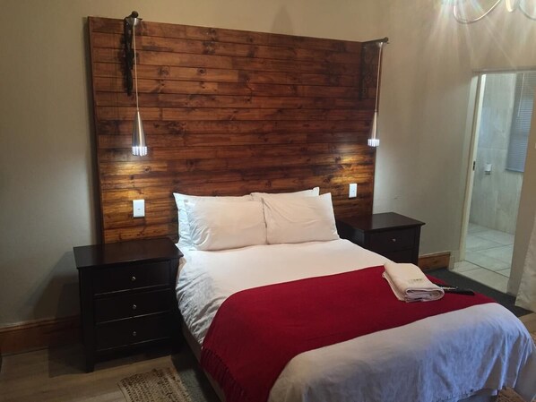 A bedroom with a wooden headboard, two bedside tables, a bed with white bedding and a red blanket, and a nightstand with a lamp. - Tranquil House Bed and Breakfast (Komani)