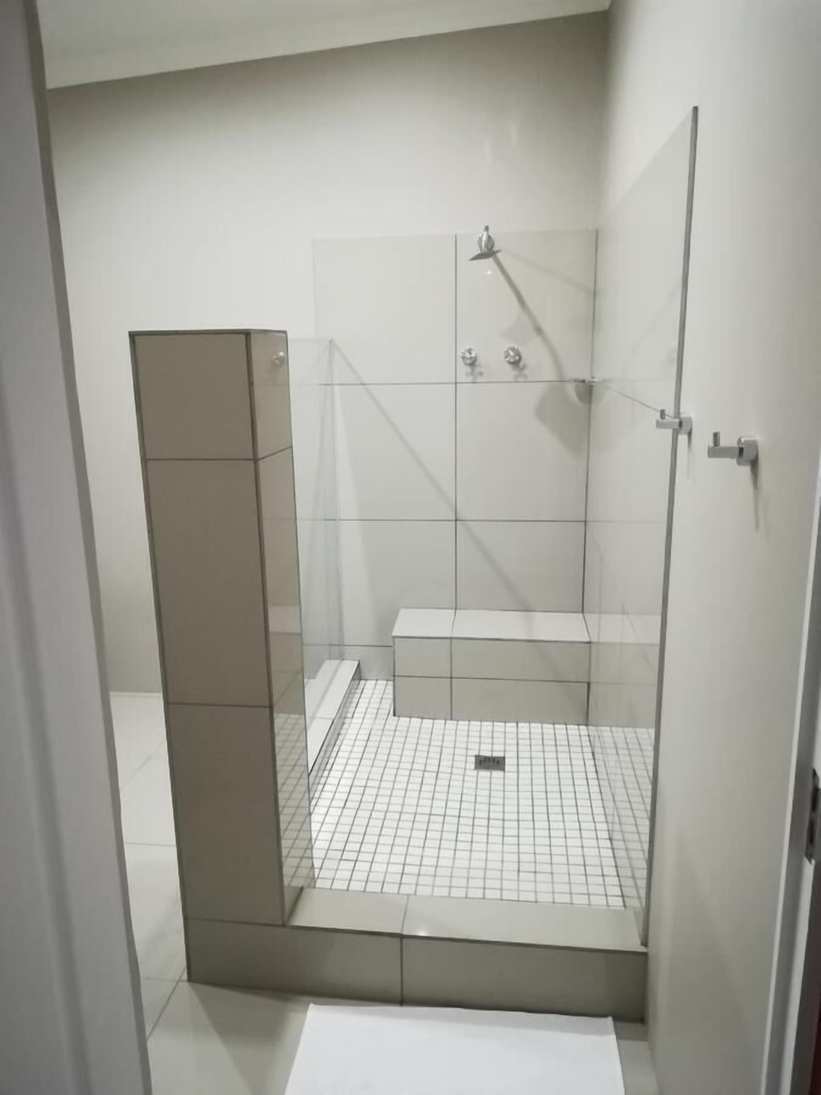 A small, enclosed shower area with a glass door, tiled floor, and a bench.