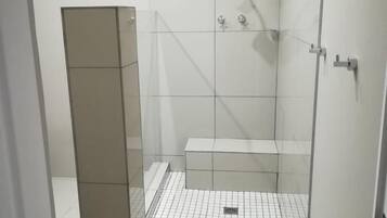 A small, enclosed shower area with a glass door, tiled floor, and a bench.