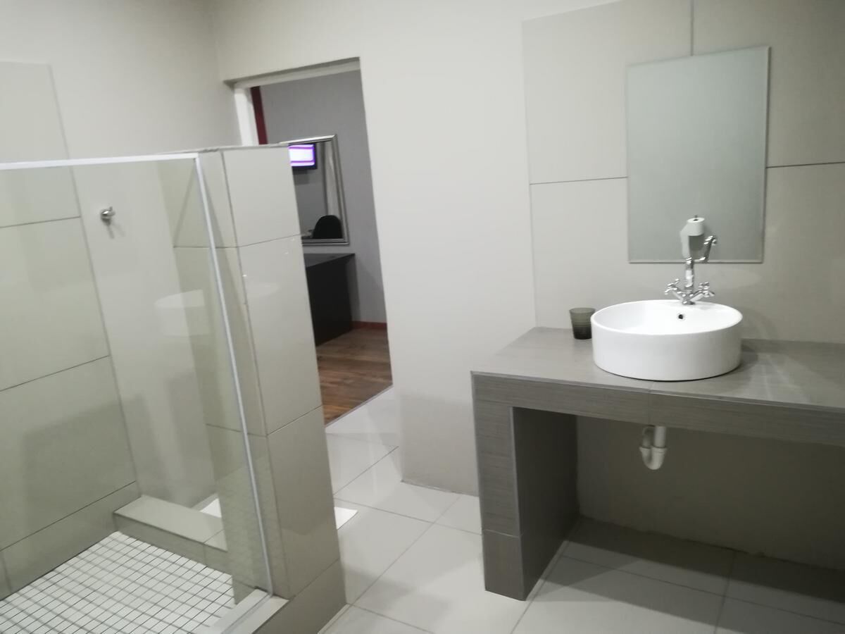 Ein modernes Badezimmer mit einer Glaskabine zur Dusche, einem weißen Waschbecken und einem Spiegel darüber.