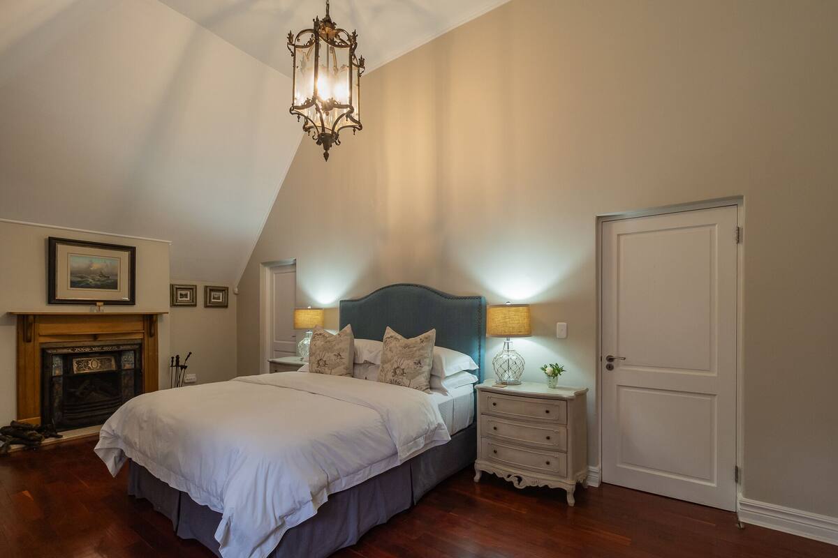 Un dormitorio con una cama grande, chimenea, candelabro y una puerta.