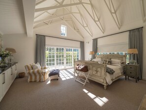 Ruime slaapkamer met een groot bed, een kleine zithoek en een dressoir. Er is een raam met uitzicht op groen.