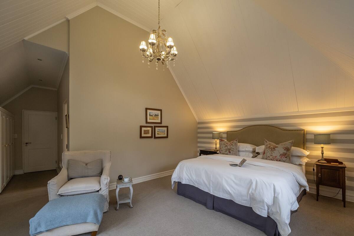 Un dormitorio con una cama grande, una silla, una mesita y un candelabro.