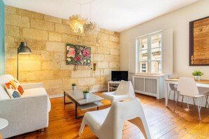 A modern living room with a stone wall, a flat-screen TV, white furniture, and a large window.