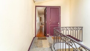 A narrow hallway with a wooden floor, a red door, and a metal railing.