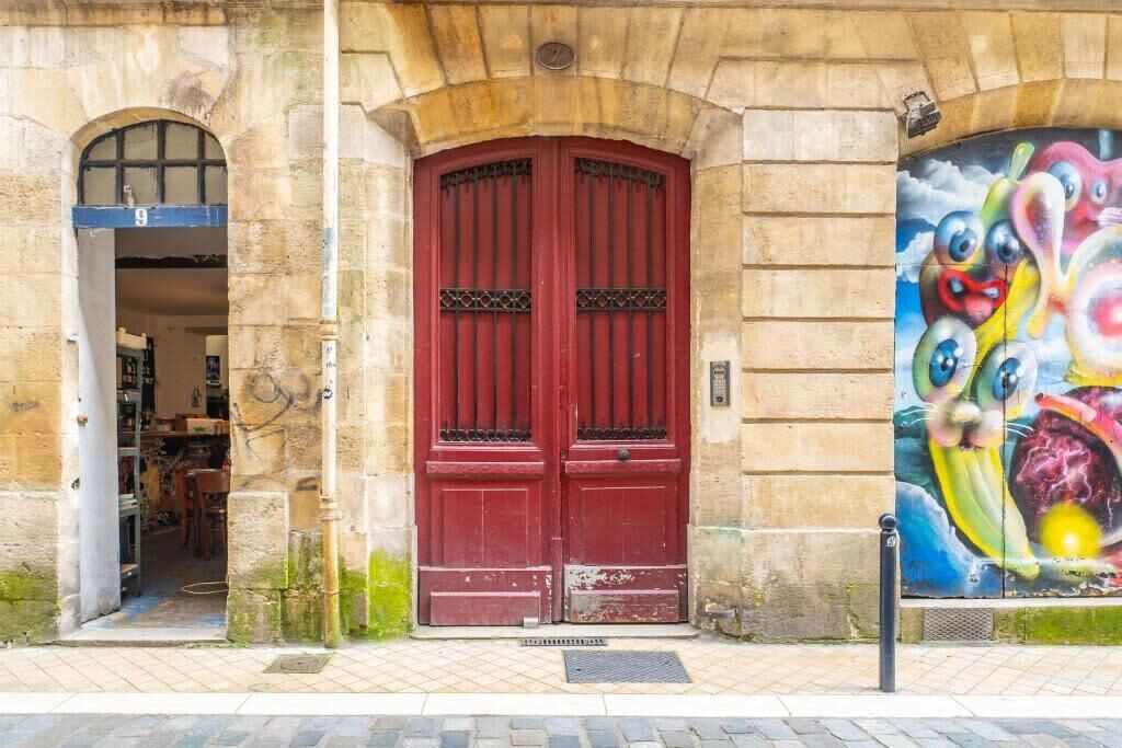 A red double door with a metal grille, set in a stone building with a small shop entrance to the left.