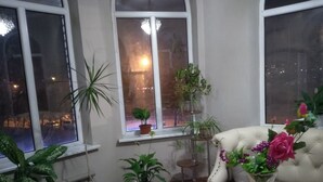 Une pièce dotée d’une grande fenêtre, de nombreuses plantes en pot, d’un canapé blanc et d’un vase rempli de fleurs.
