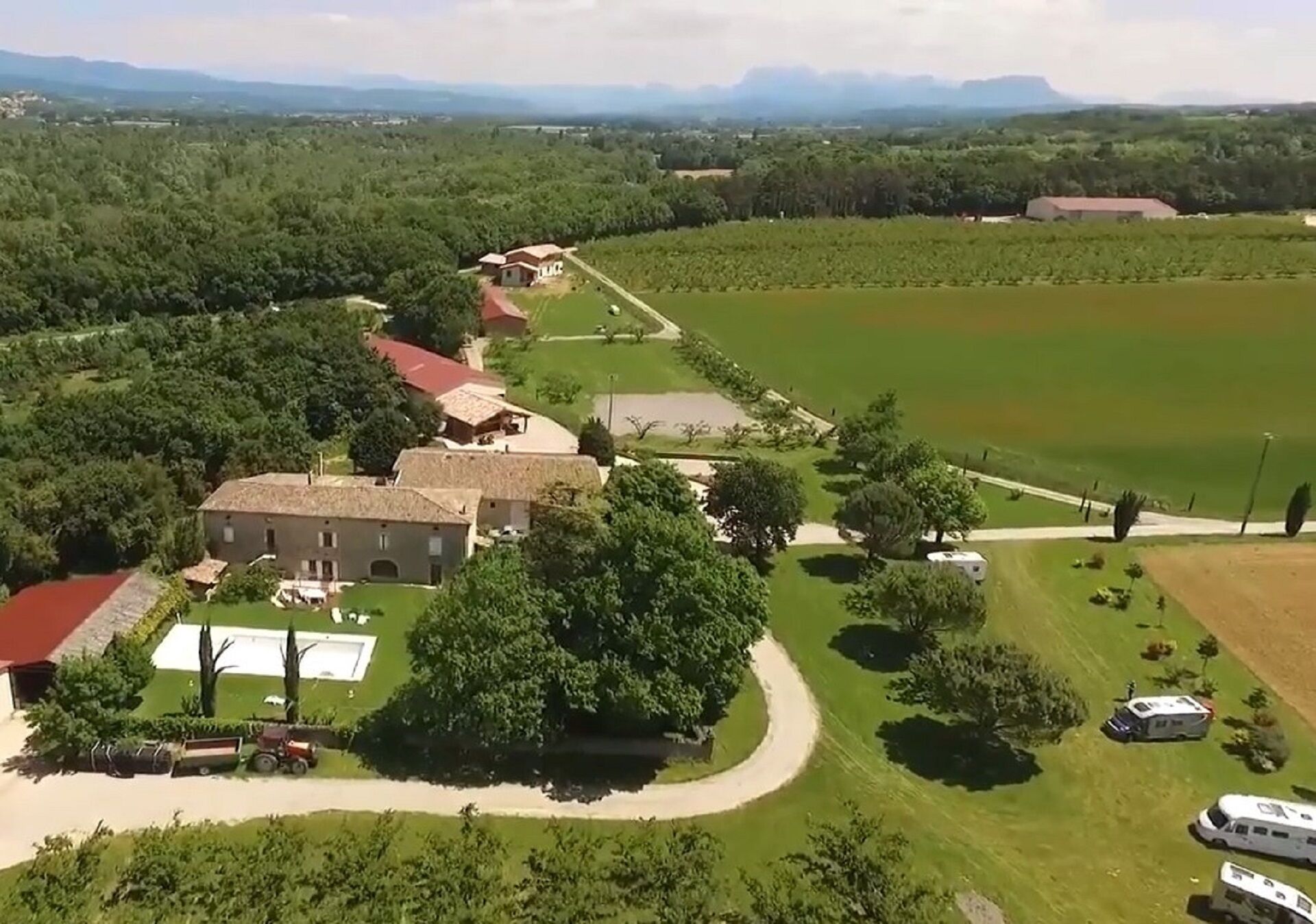 An aerial view of a property with a large building, a swimming pool, and several RVs parked on the lawn.