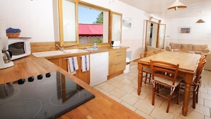 A kitchen with a stove, microwave, sink, and wooden cabinets. There is a dining table with chairs and a window with a view of the outside. - Cottage 8 ps. 3 cbres. Swimming pool. Center Drôme, ideal for discovering Drome and Ardéche (Grane)