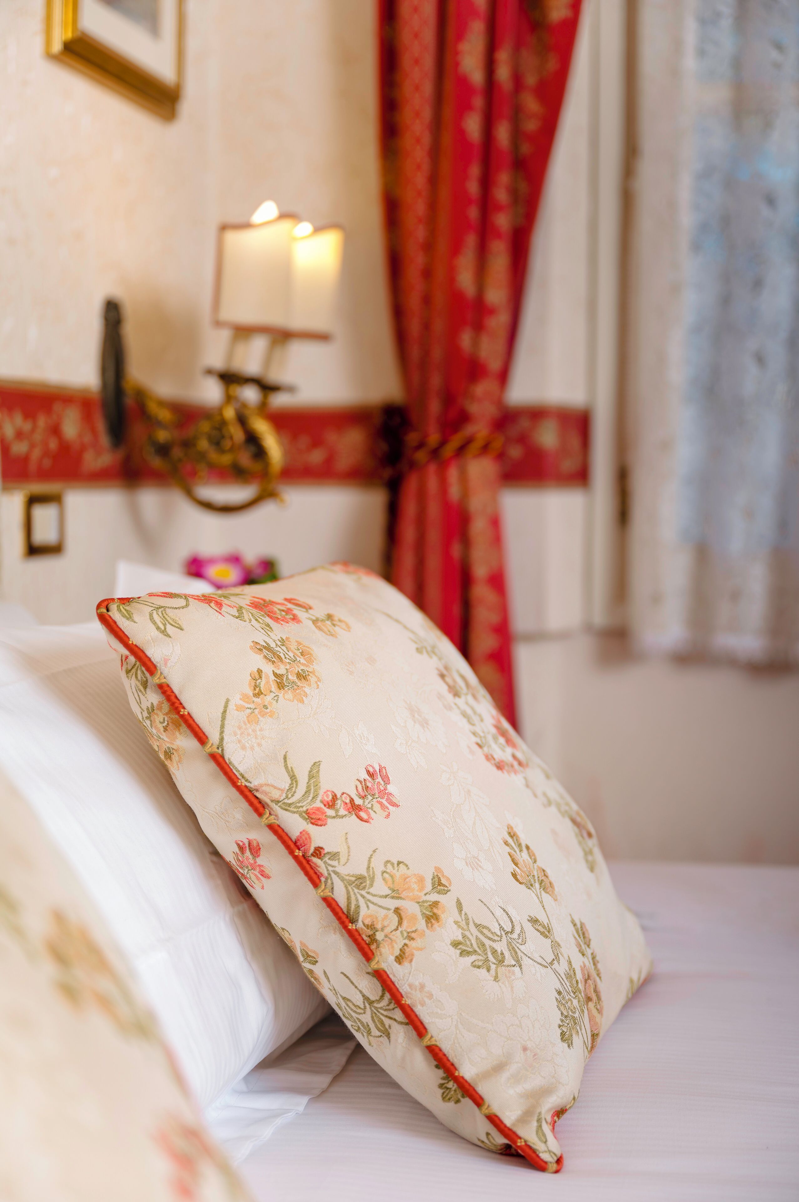 Una cama con almohadas de estampado floral y una mesita de noche con lámpara.