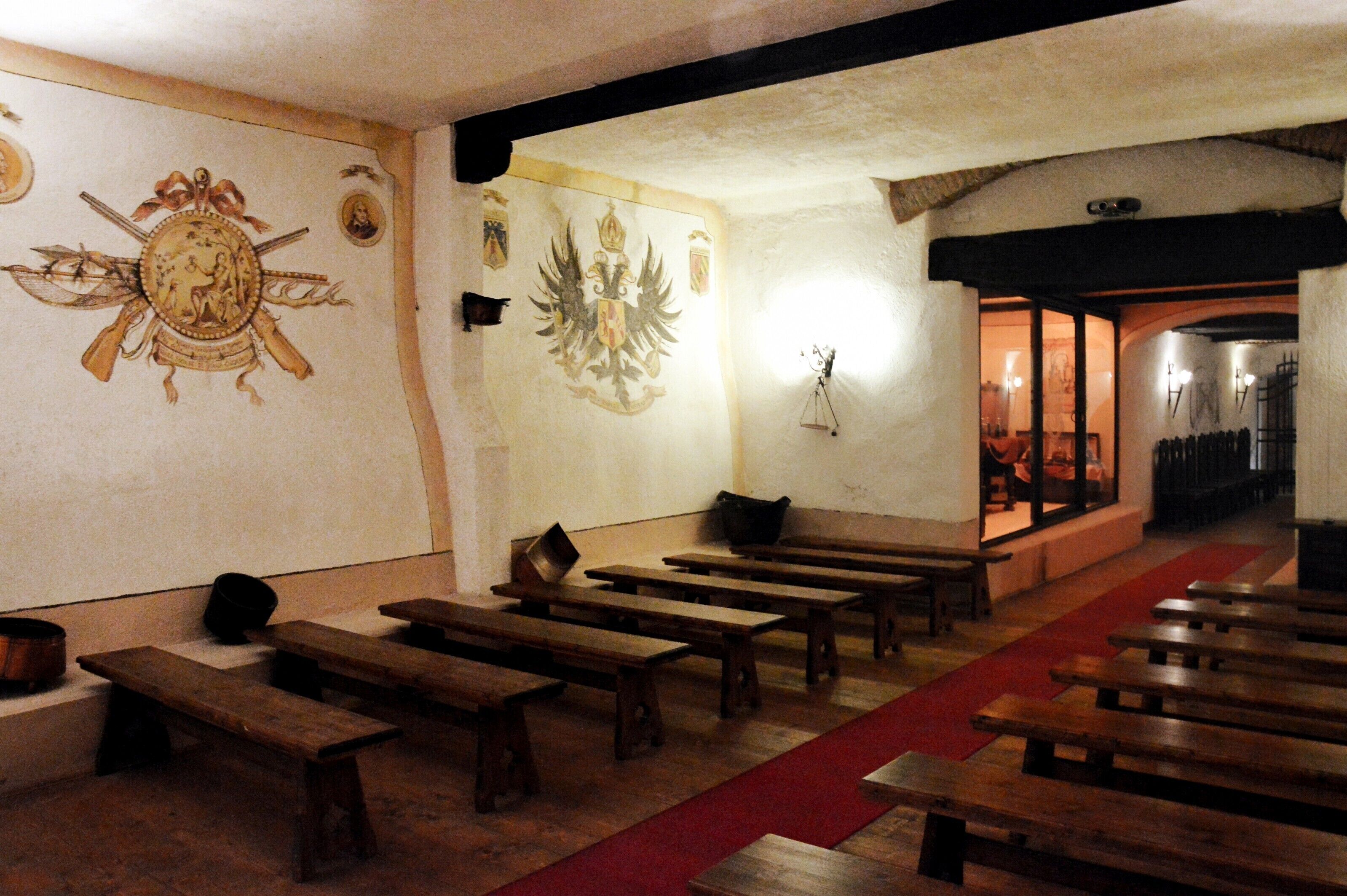 Interno di una chiesa con bancali di legno, un tappeto rosso e opere d'arte religiose alle pareti.