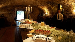 A dimly lit stone-walled room with tables set for a meal, featuring floral decorations and candles.