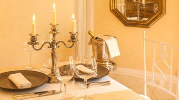 Una mesa de comedor dispuesta con velas, copas y cubiertos, con un espejo y detalles ornamentales en el techo.