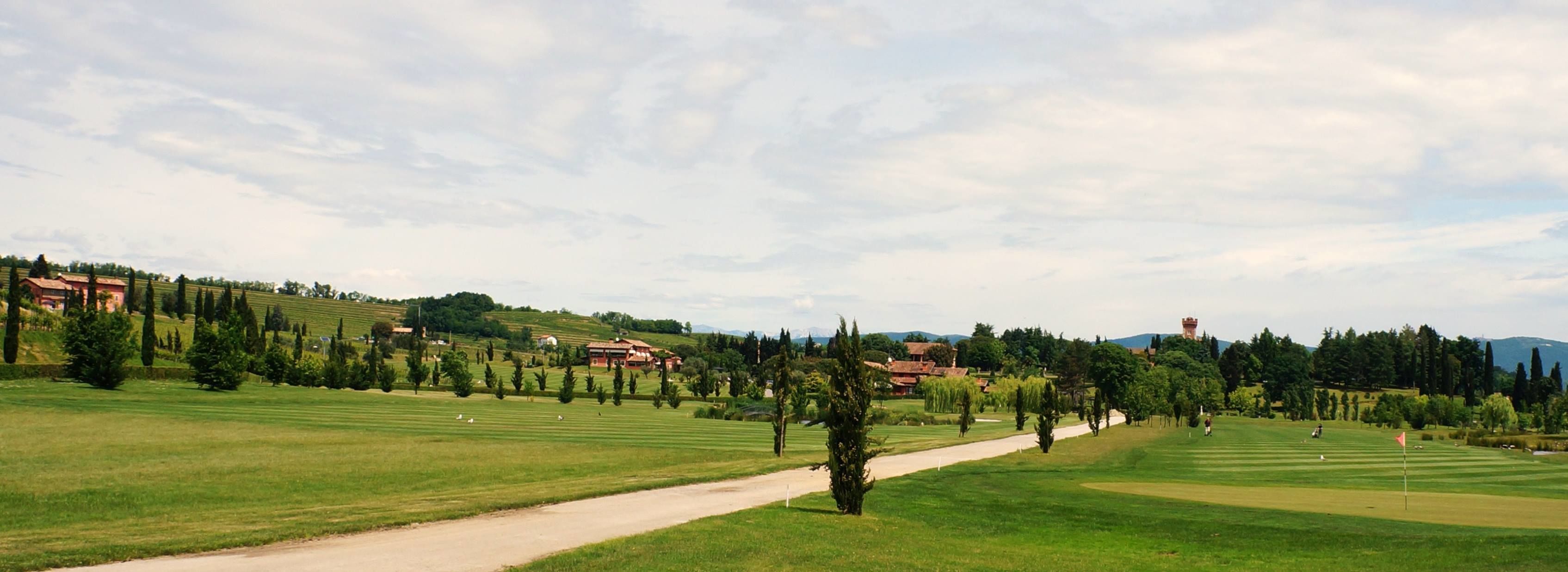 A golf course with a clear path, green fields, and distant buildings.