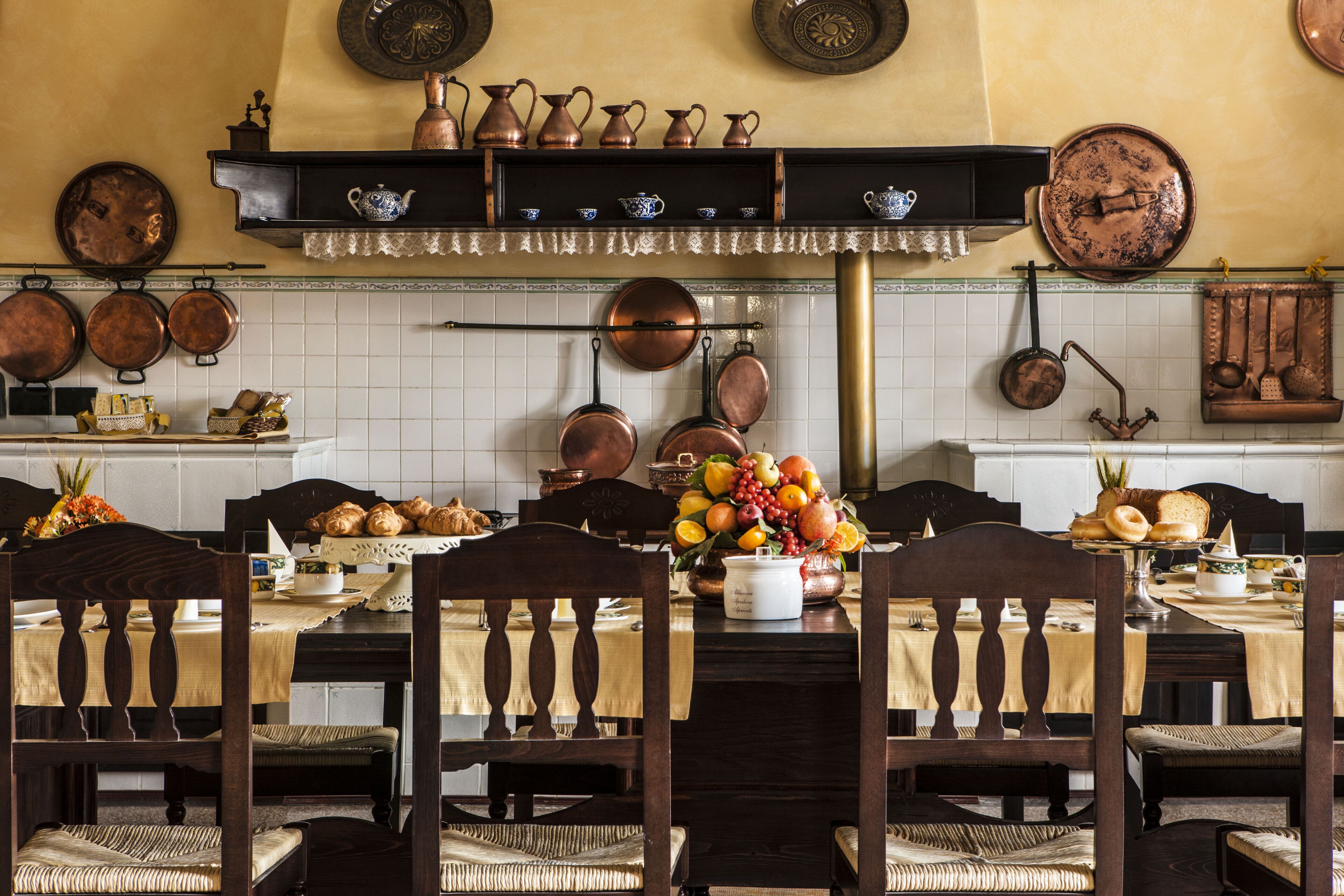 Un comedor con una mesa de madera, sillas y varios utensilios de cocina de cobre colgados en la pared.
