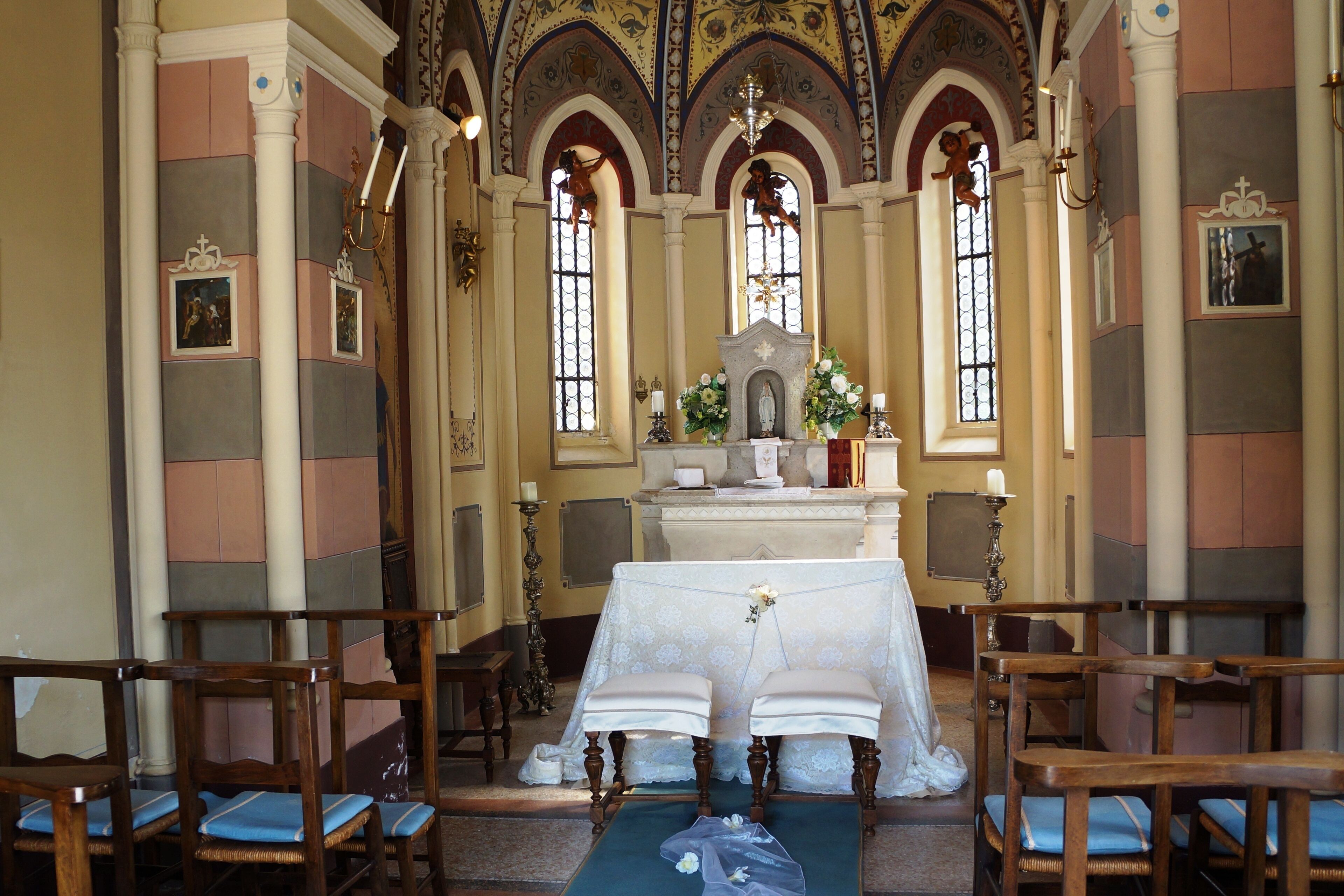 Un interior con un altar central, bancales y una araña.