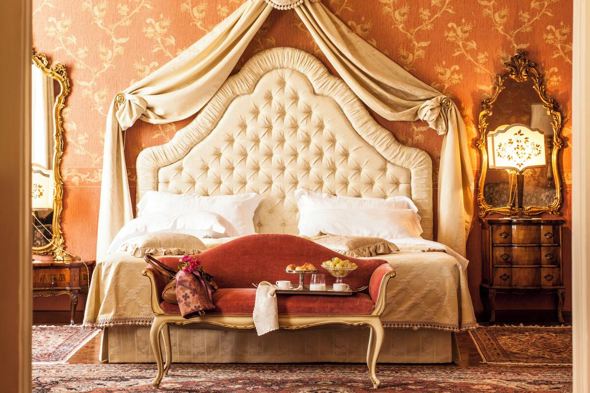 Un dormitorio lujoso con cama con dosel, una chaise longue y una mesita de noche con lámpara.
