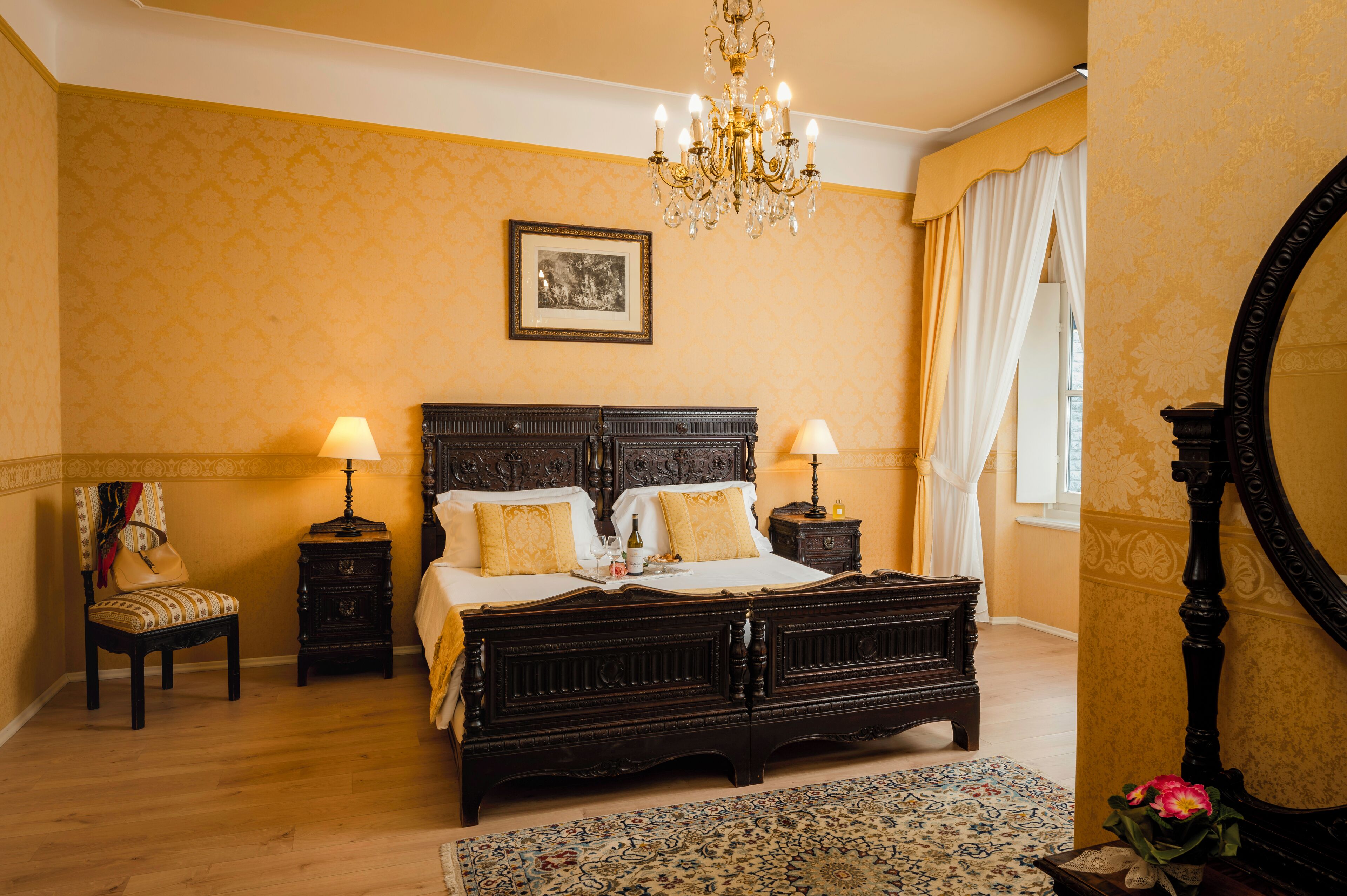 A classic bedroom with a four-poster bed, two bedside tables, a chandelier, and a large mirror.
