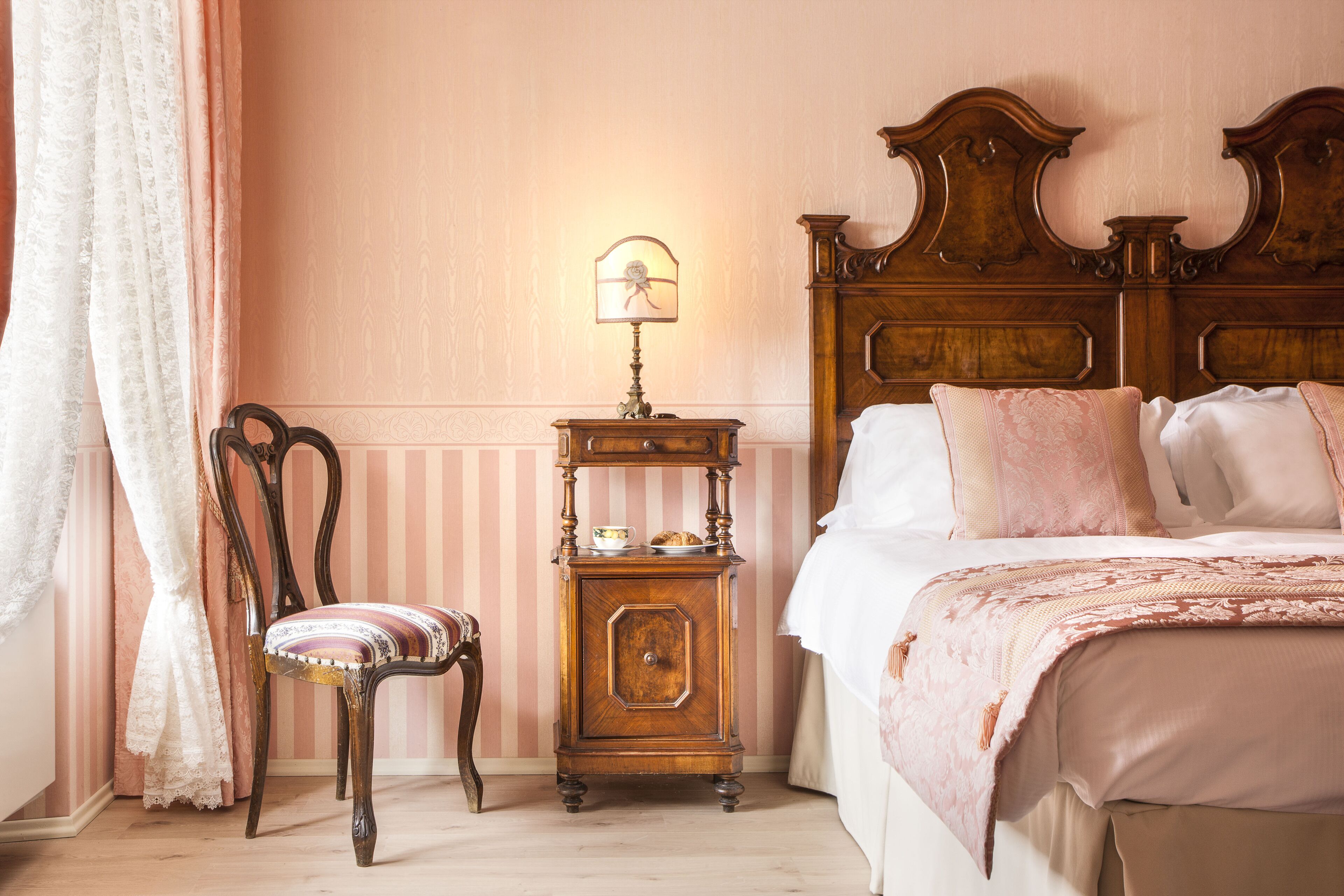 A bedroom with a wooden headboard, a bedside table with a lamp, a chair, and a bed with pillows.