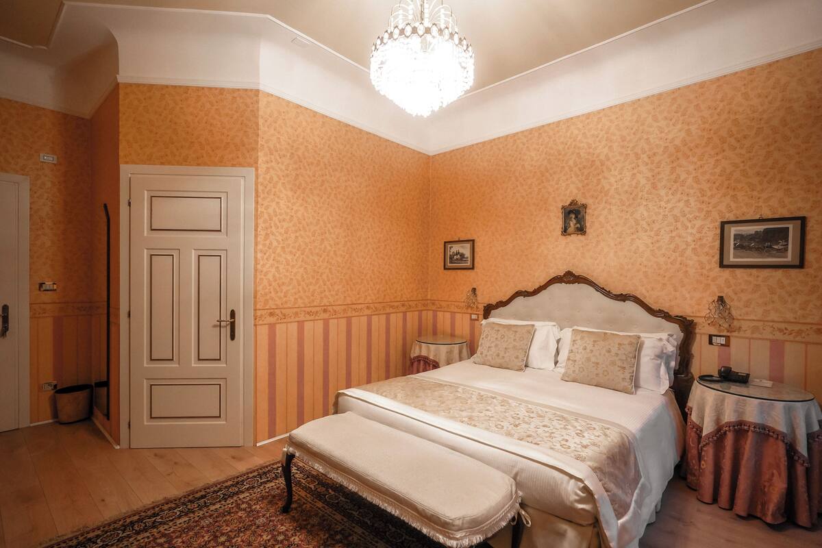 Un dormitorio con una cama grande, una araña, una mesita de noche y una puerta.
