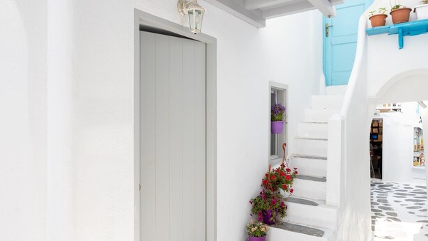A narrow, white-walled street with a blue door and steps leading to a higher level.