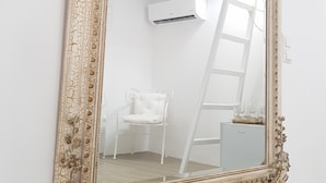 A large ornate mirror with a distressed gold frame, a white chair, and a ladder in a room with white walls and ceiling.