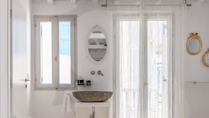 A bedroom with a large bed, a round mirror, a stone basin sink, and sheer curtains.