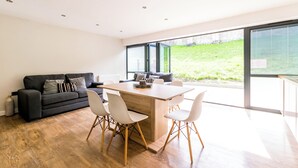 A modern living space with a wooden dining table, white chairs, a black sofa, and a large window offering a view of a grassy area. - City Apartments Monkbar Mews (York)