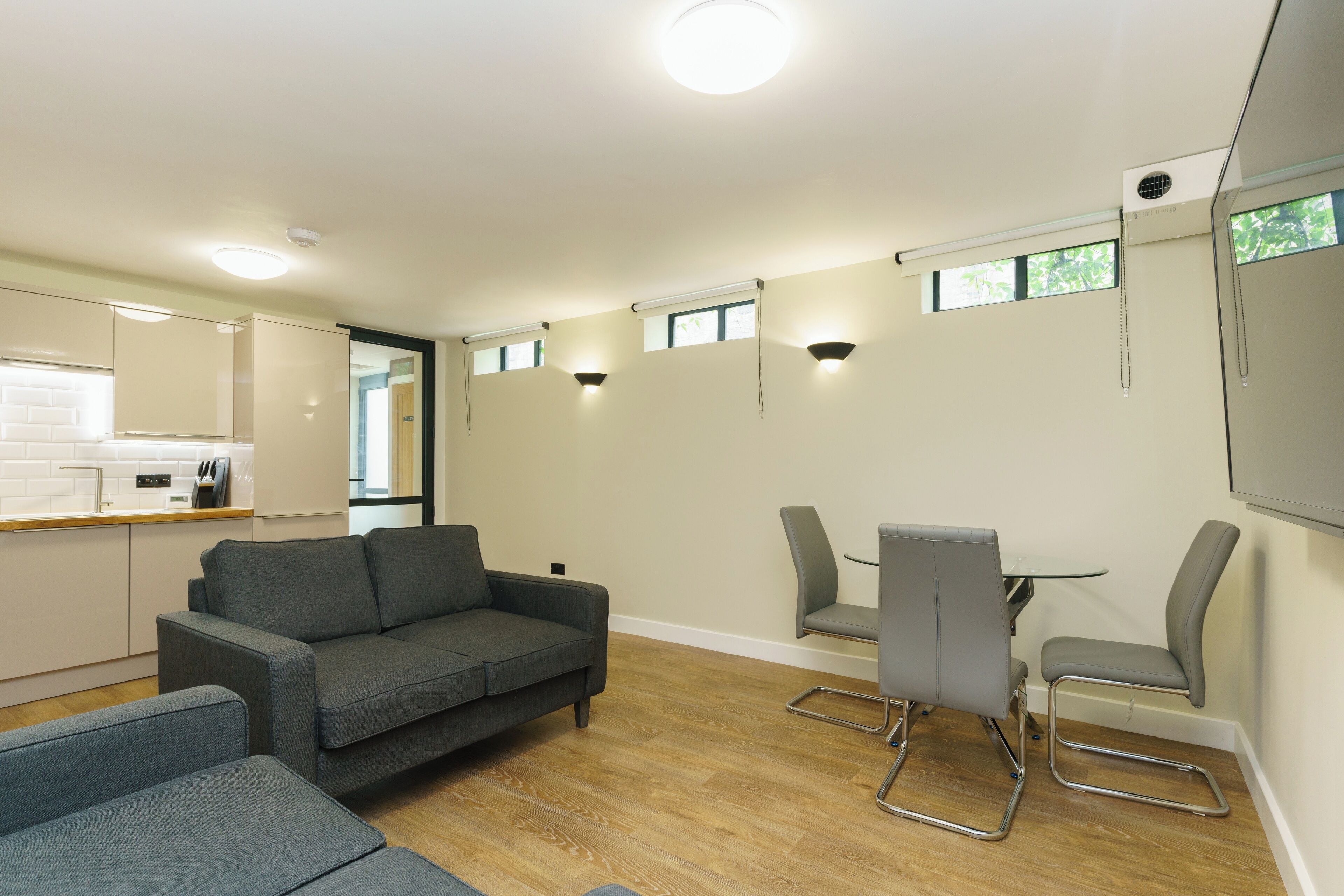 A modern living room with a grey sofa, a dining table with chairs, and a kitchen area with a white countertop.