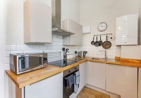 A modern kitchen with white cabinets, a stainless steel microwave, a wooden countertop, a stove, and a clock on the wall.