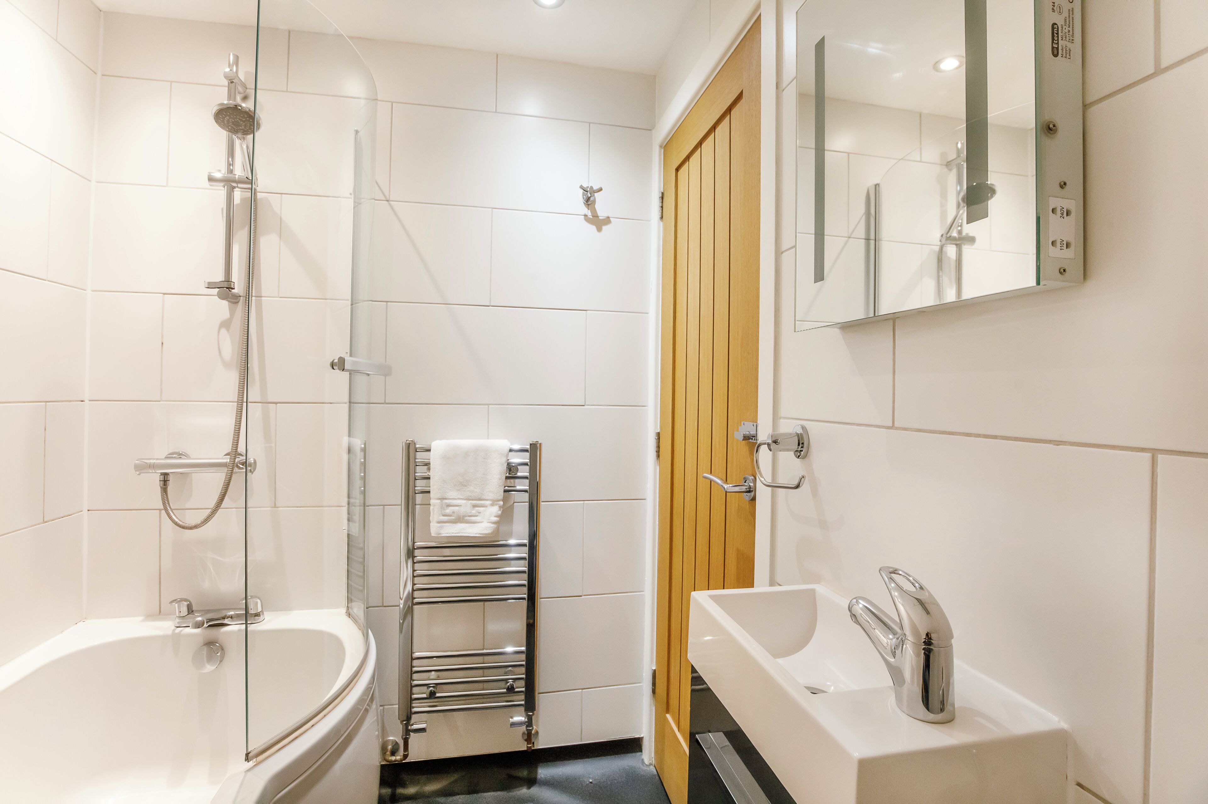 A modern bathroom with a glass-enclosed shower, a freestanding bathtub, a vanity with a sink and mirror, and a towel rack with a towel.