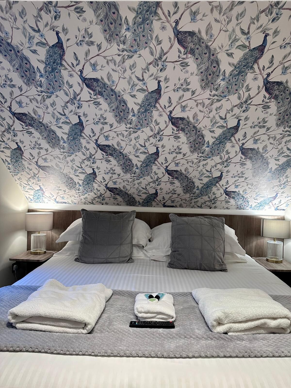 A hotel room with a bed, grey pillows, and a blanket.