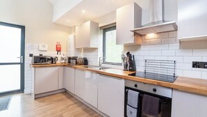 A modern kitchen with white cabinets, a wooden countertop, a built-in oven, and a window with blinds. - City Apartments Monkbar Mews (York)