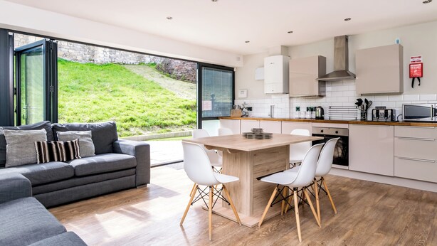 A modern kitchen with a dining area, large windows, and a view of a grassy hill. - City Apartments Monkbar Mews (York)