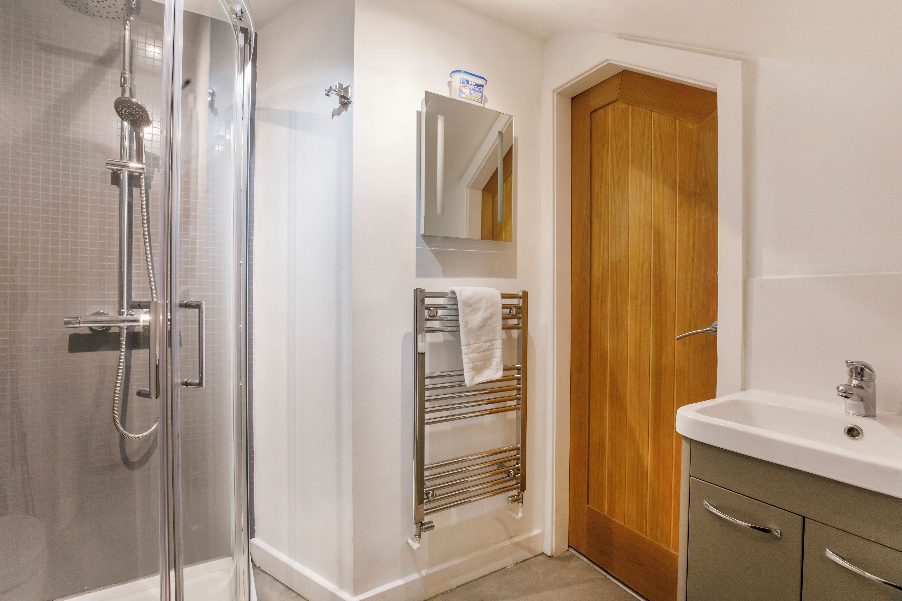 A bathroom with a glass-enclosed shower, a wooden door, a white sink, and a towel rack.