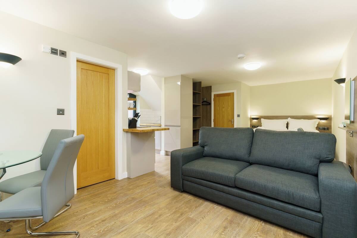 Una sala moderna con un sofá gris, una mesa de vidrio y una puerta de madera.