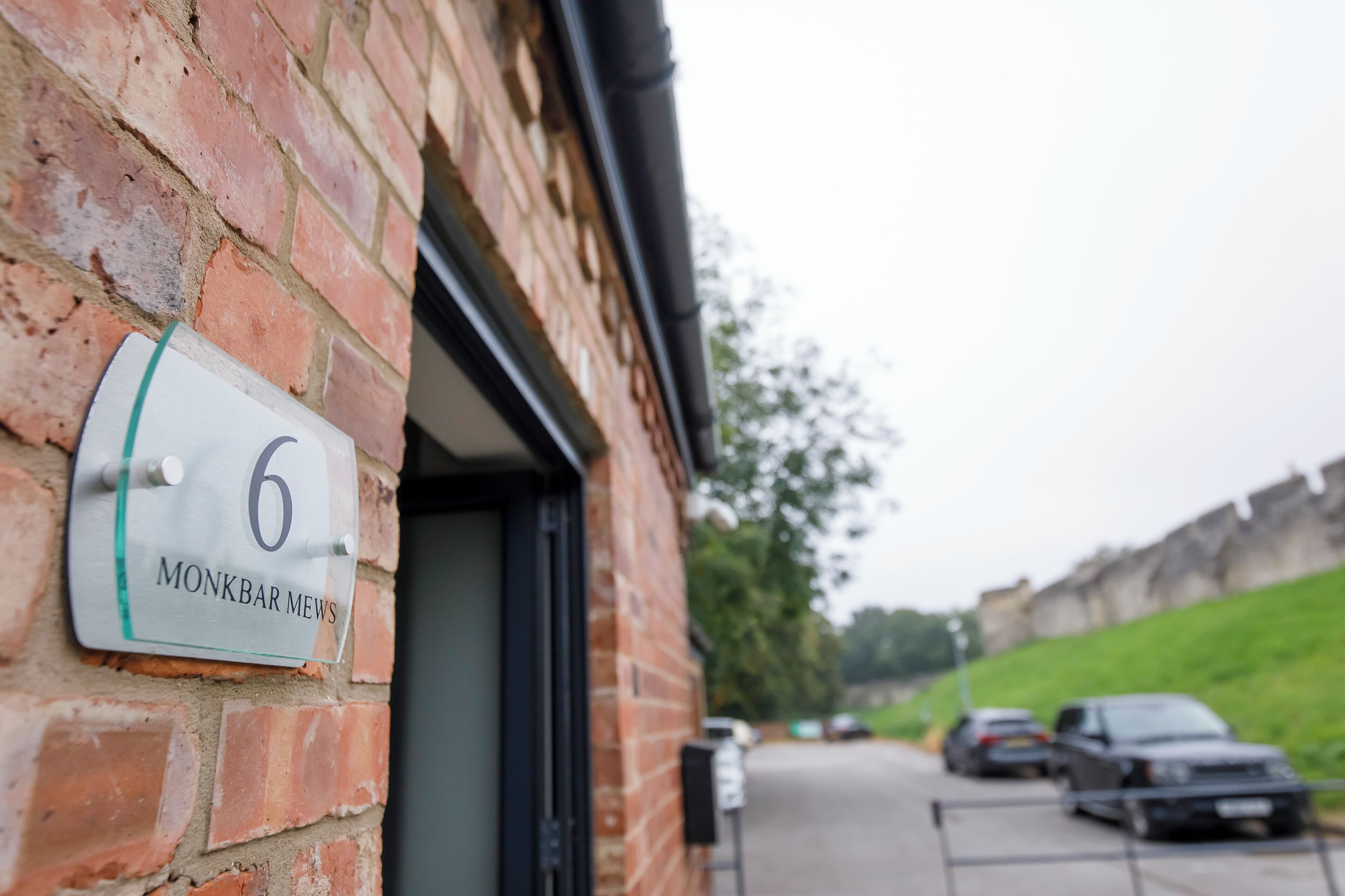 A brick building with a sign reading "6 MONKBAR MEWS" and a parking area with cars.