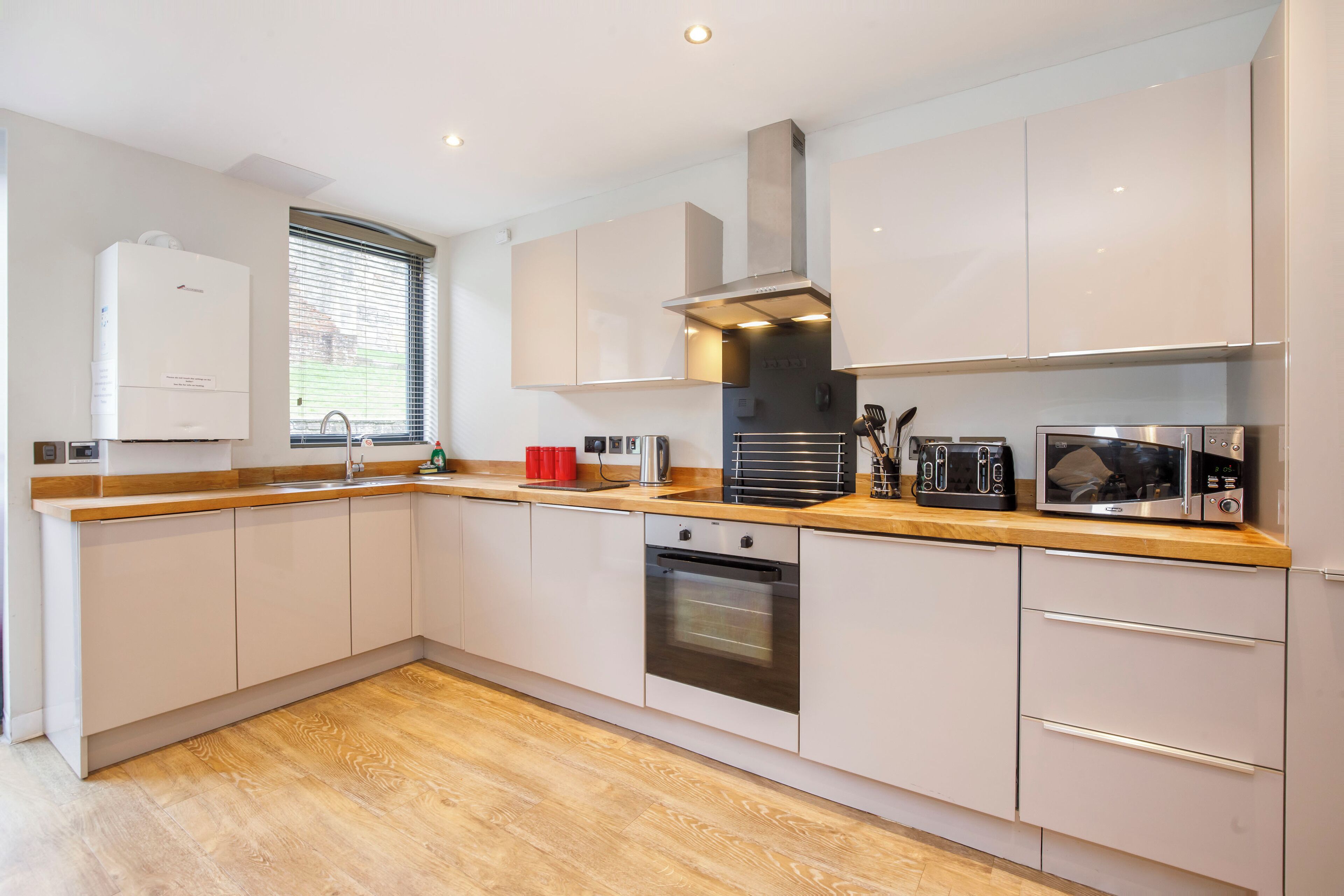 A modern kitchen with white cabinets, a stainless steel range hood, a built-in oven, and a wooden countertop.