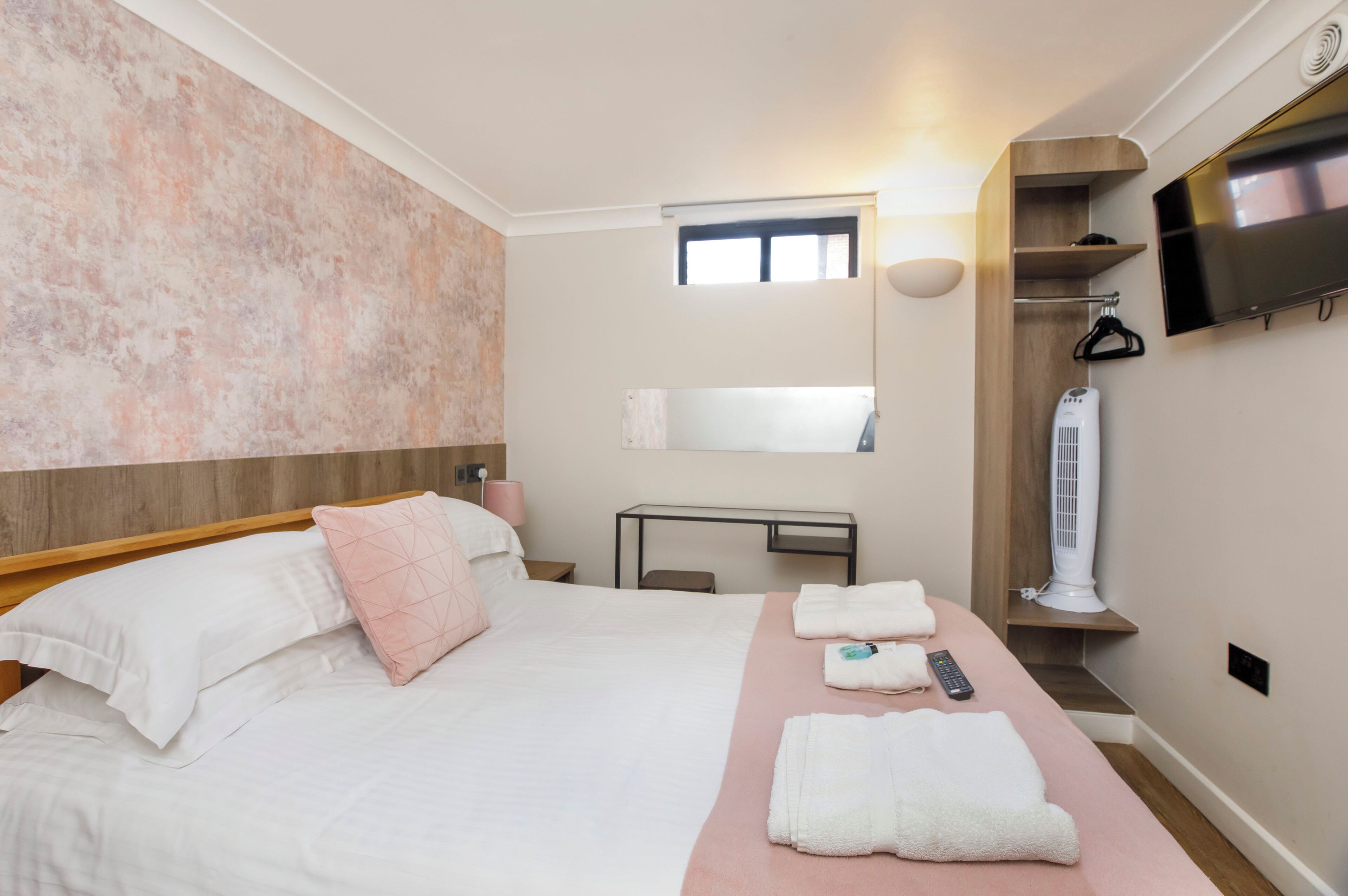 A hotel room with a bed, a desk, a TV, and a towel rack.