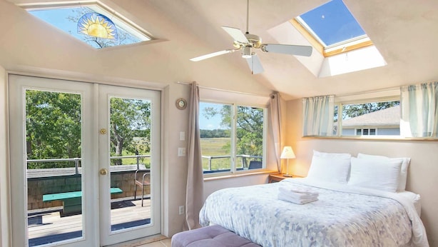 Un dormitorio con cama, ventilador de techo, tragaluz y vistas a una terraza y zona exterior.