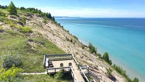 A wooden deck with chairs overlooking a coastal landscape. - Spruce at Lake Bluff Preserve-Lake Michigan Views-Sleeps 20  (Frankfort)