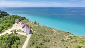 A coastal property with three white buildings with red roofs, situated on a hillside overlooking a turquoise sea. - Spruce at Lake Bluff Preserve-Lake Michigan Views-Sleeps 20  (Frankfort)