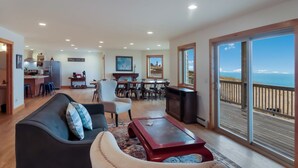 A spacious living area with a dining set, a kitchen in the background, and a large sliding glass door to the outside. - Spruce at Lake Bluff Preserve-Lake Michigan Views-Sleeps 20  (Frankfort)