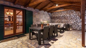 Un espacio exterior para comer con pared de piedra y techo de madera, que incluye una mesa, sillas y una chimenea de piedra.
