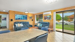 Een moderne woonkamer met twee leren banken, een eettafel en een groot raam met uitzicht op een parkeerplaats.