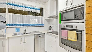 Een moderne keuken met witte kasten, een roestvrijstalen spoelbak, een magnetron, een oven en een afdruiprek.