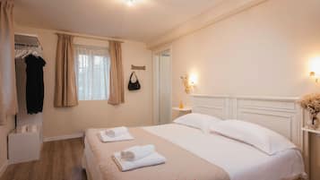 Una habitación de hotel con una cama, un armario, un ventanal con cortinas, una mesita de noche con lámpara y un espejo montado en la pared.