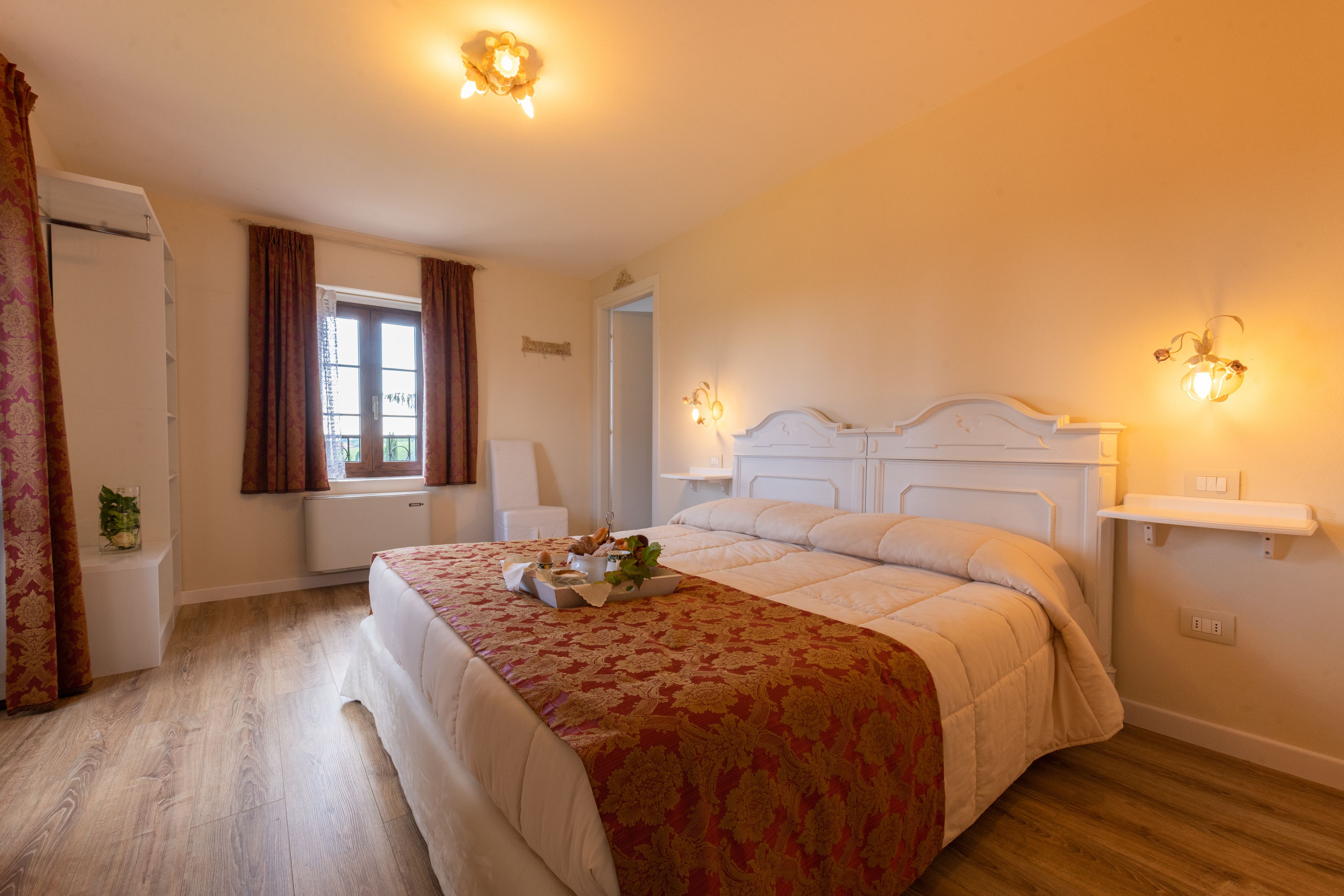 Ein Schlafzimmer mit einem großen Bett, einem Fenster mit Vorhängen, einem Nachttisch und einer wandmontierten Lampe.